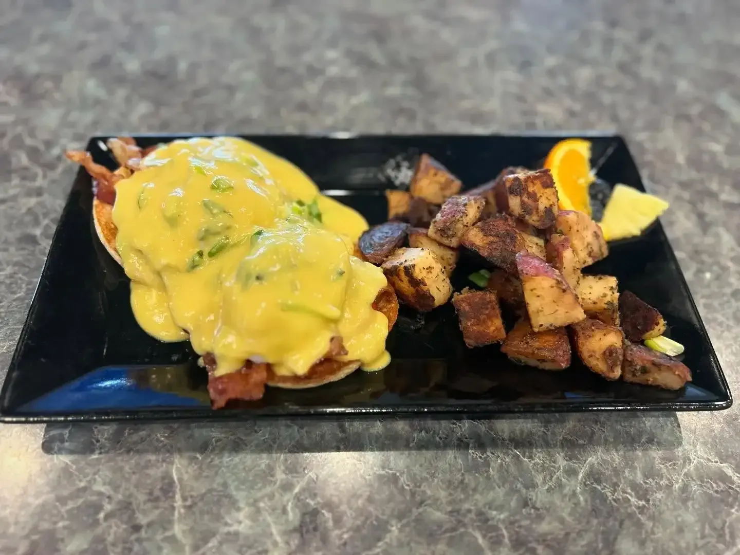 A plate of food with eggs benedict and potatoes on a table.