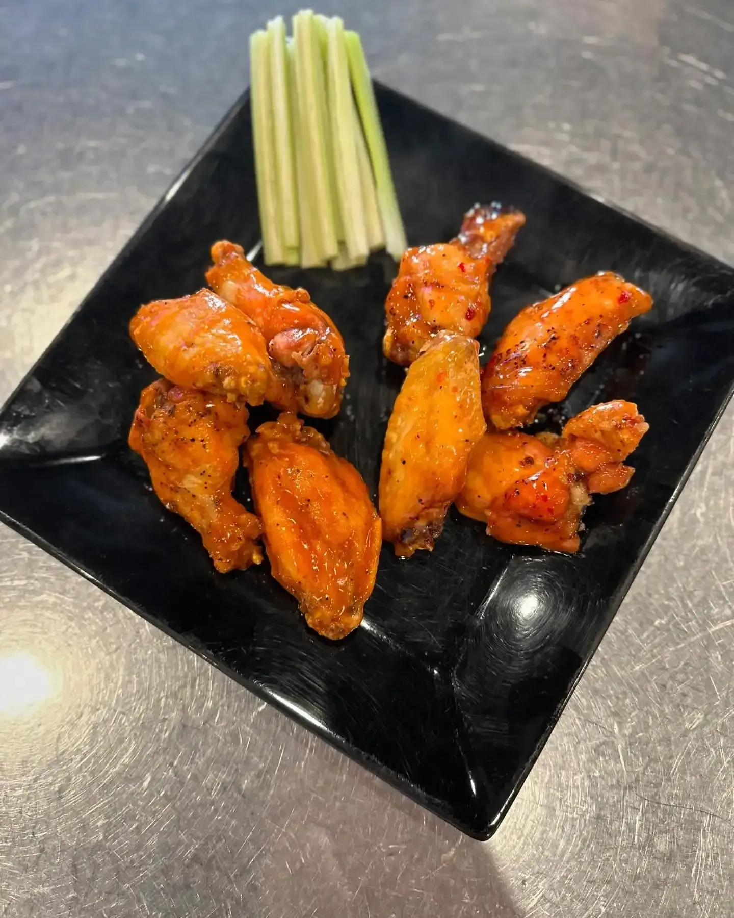 A black plate topped with chicken wings and celery sticks.