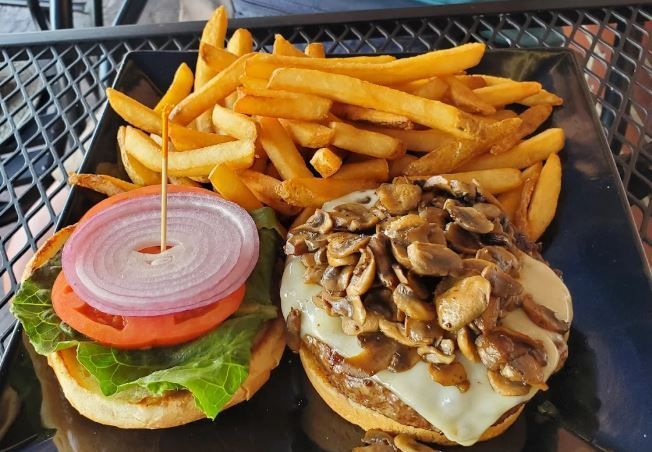 A hamburger and french fries on a black plate on a table.