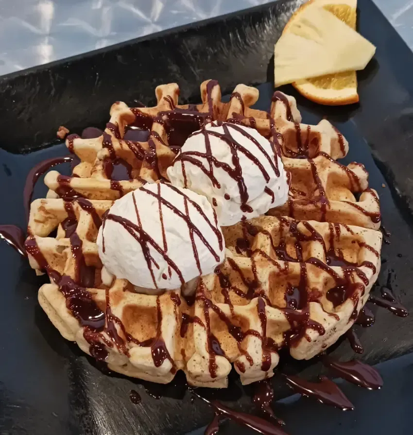 A waffle with ice cream and chocolate sauce on it