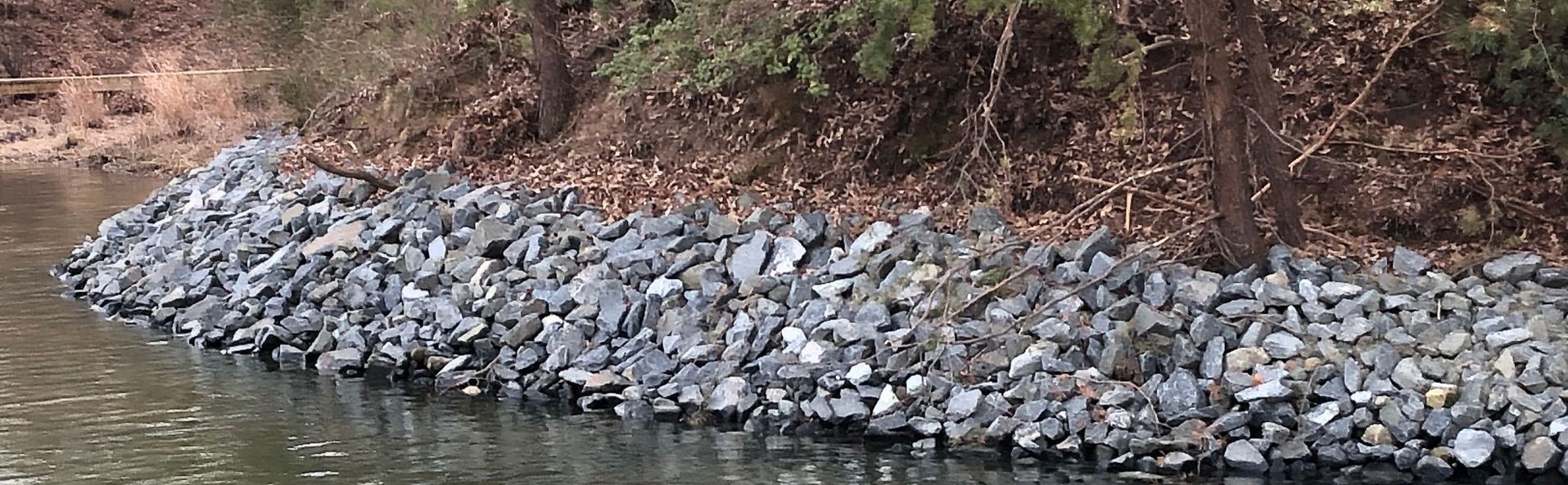 Rip Rap, a type of shoreline restoration, is sitting next to a body of water.