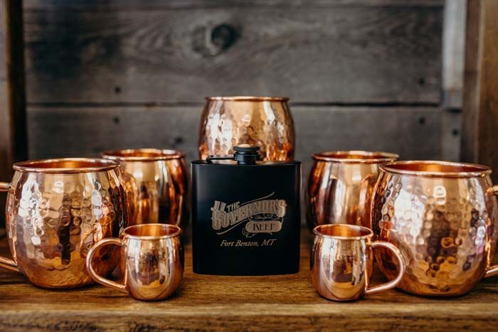 A group of copper mugs and glasses are sitting on a wooden table.