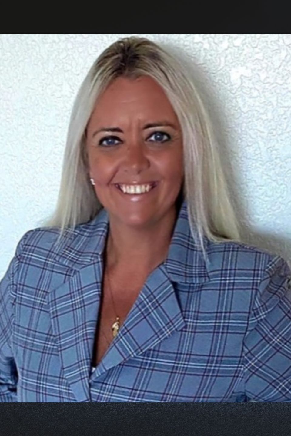 Smiling woman in a blue plaid blazer standing against a light textured wall