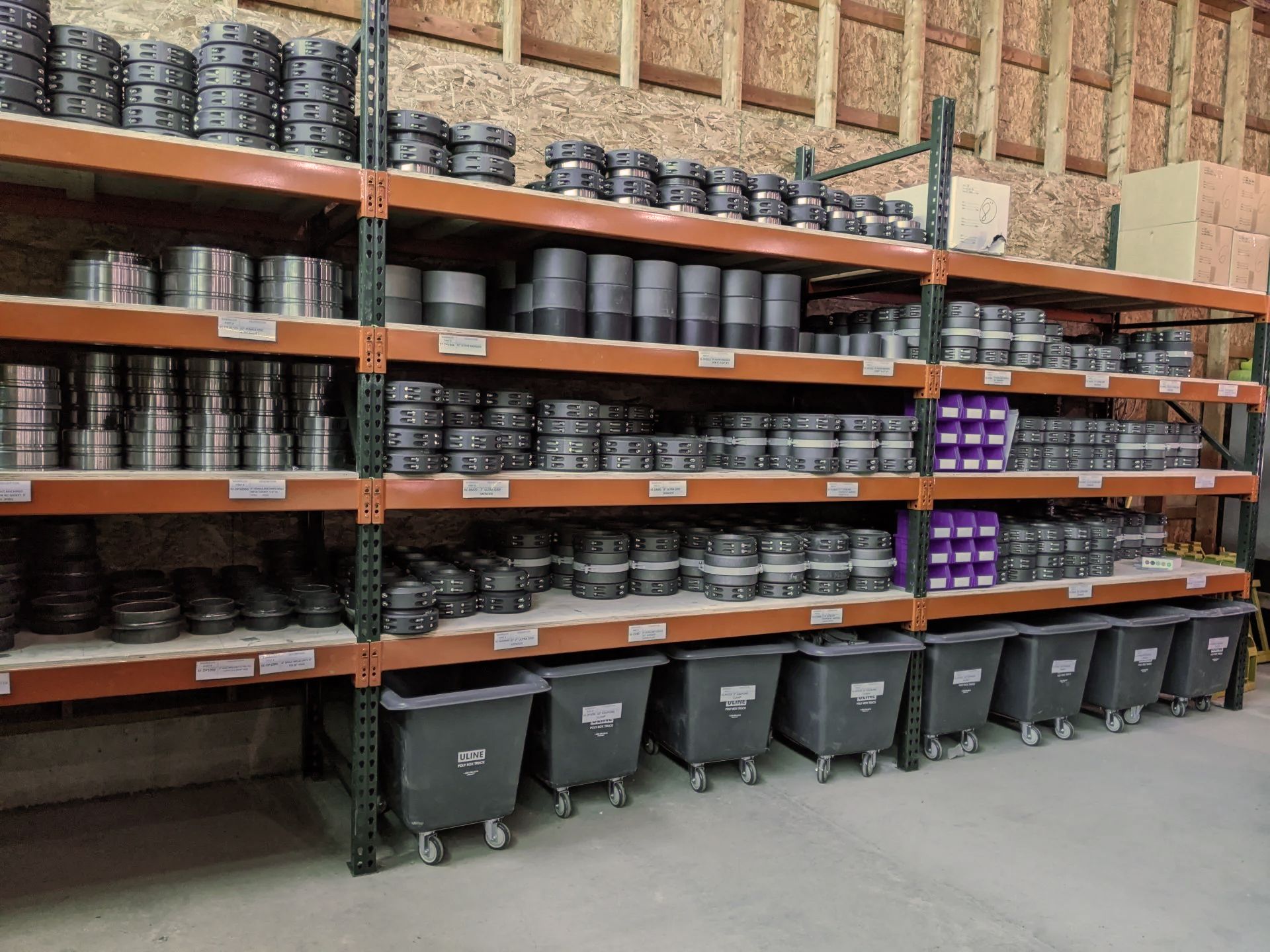 Warehouse shelves stocked with stacked black and purple containers above rows of gray bins