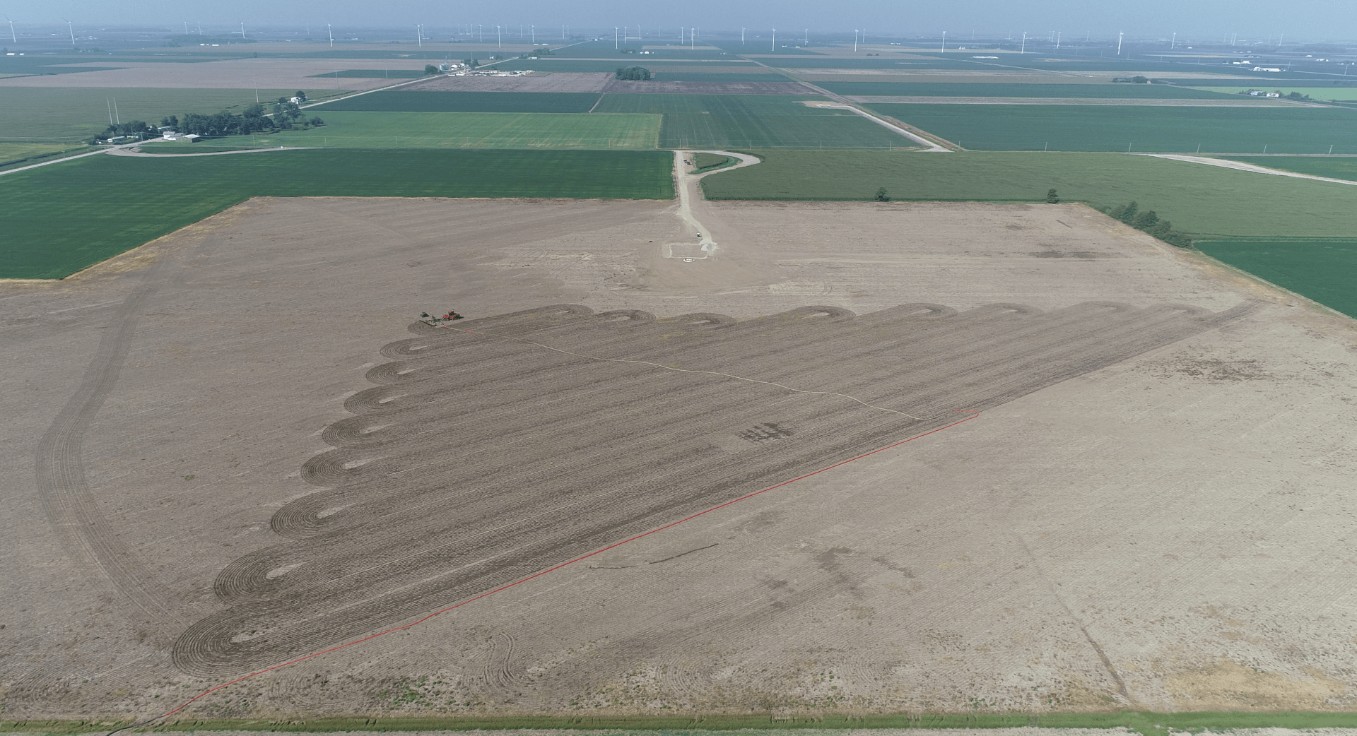 Aerial view of a large plowed field with a triangular strip of darker soil beside green farmland.