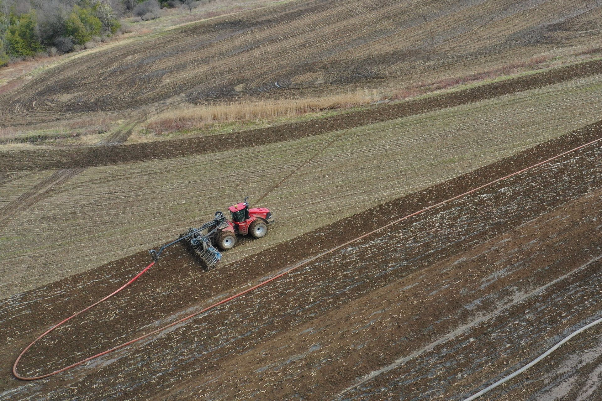 Red tractor plowing a striped field on a hillside