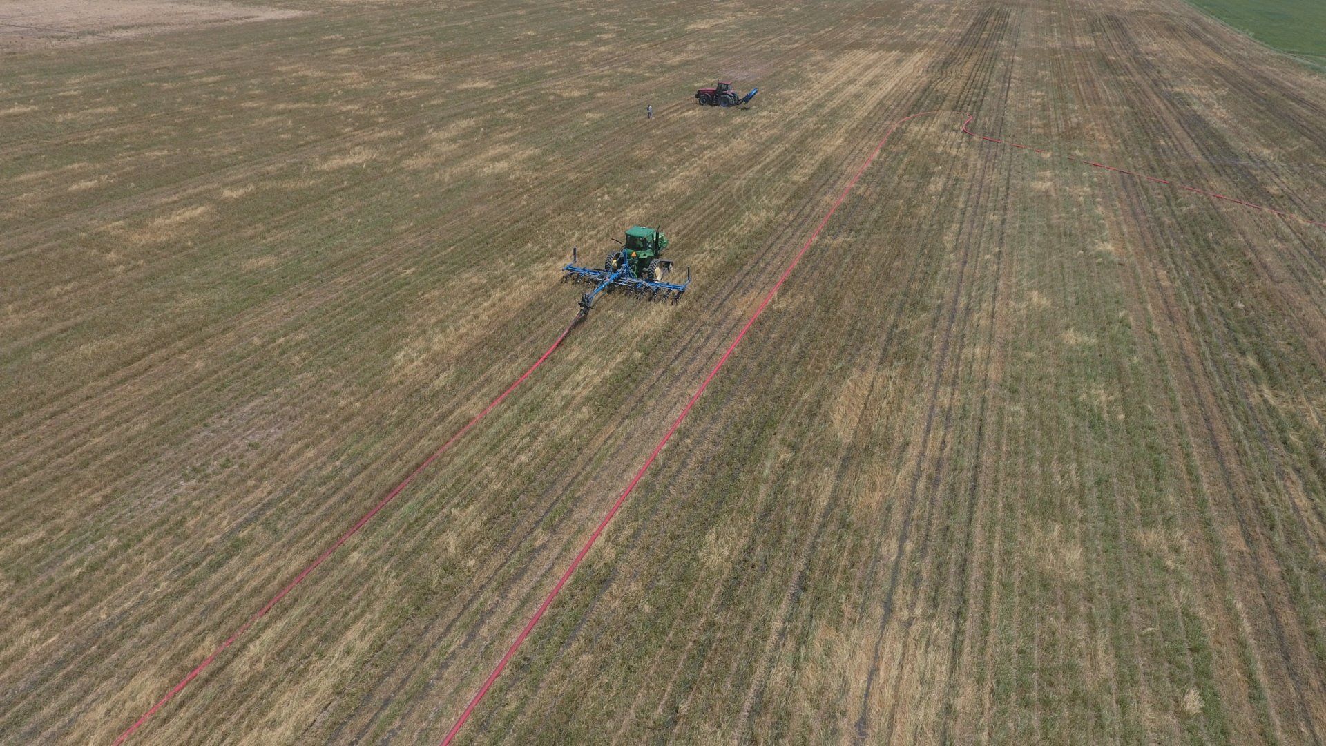 Aerial view of a green tractor working a large brown field with red guidance lines visible.