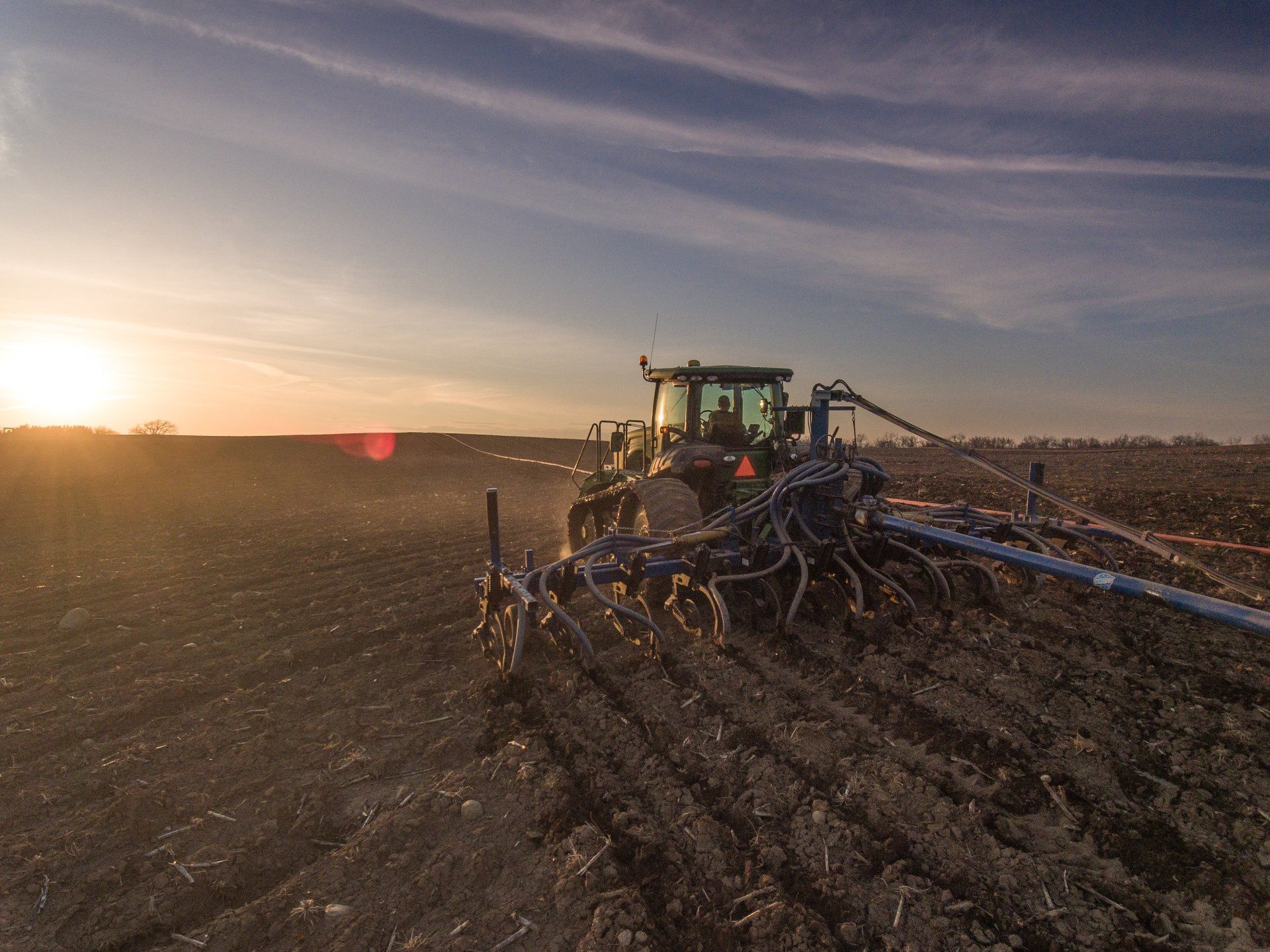 Tractor spraying a field at sunset, with dust and low golden light across the farmland.