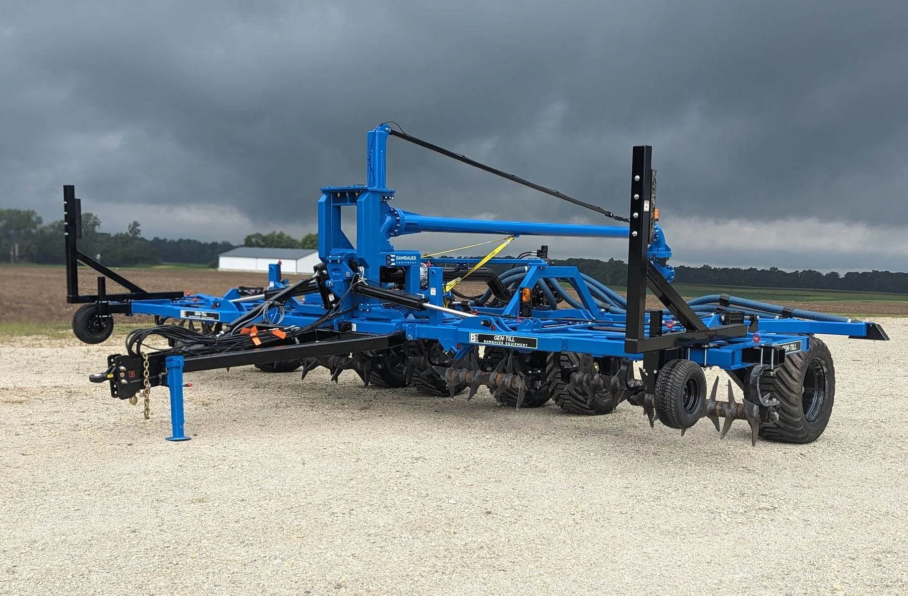 Blue agricultural implement on a gravel lot under a cloudy sky