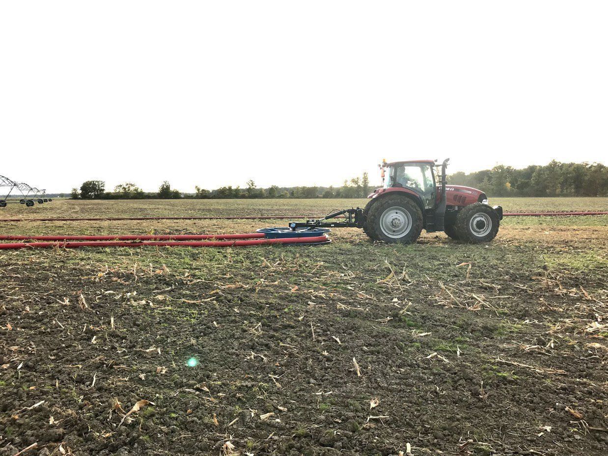 Red tractor towing farm equipment across a plowed field under a cloudy sky