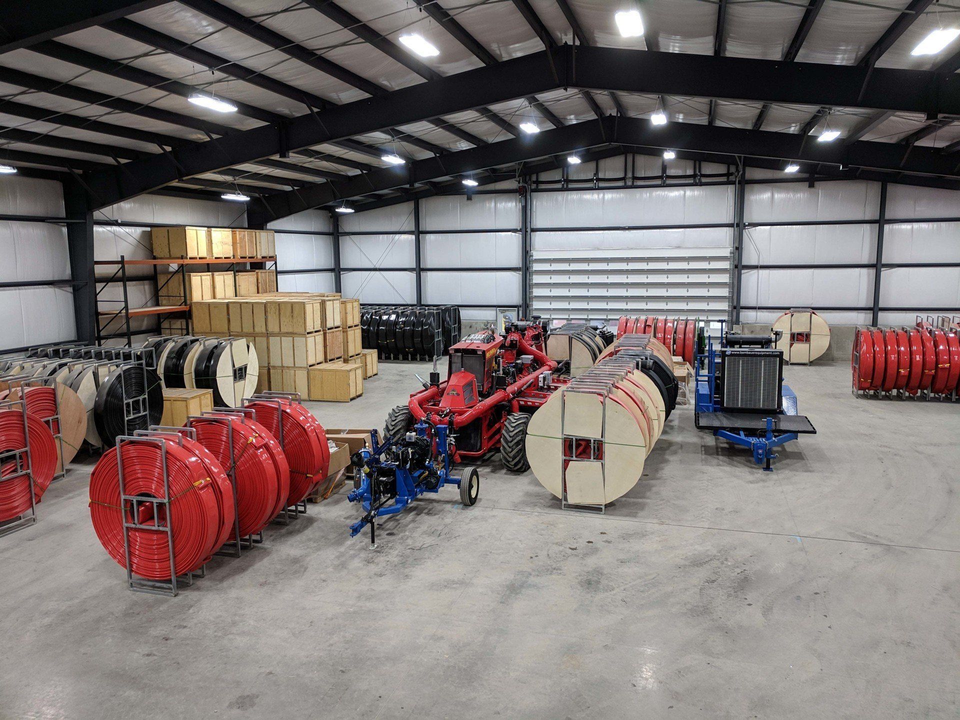 Warehouse with large red cable reels, wooden crates, and industrial equipment on a concrete floor