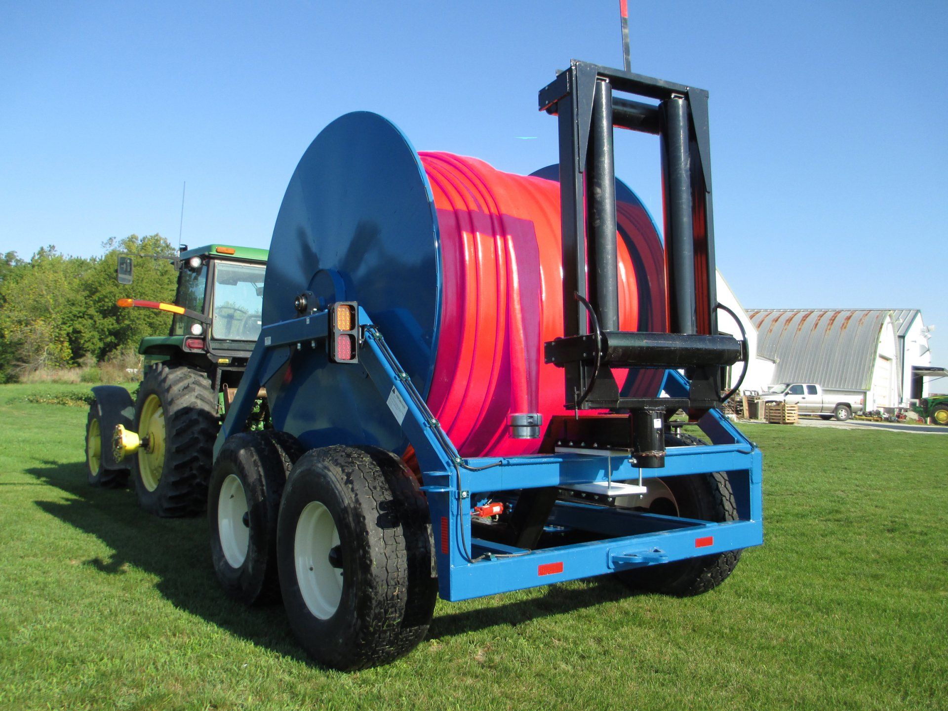 Blue hose reel trailer with a red hose attached, parked on grass behind a tractor.