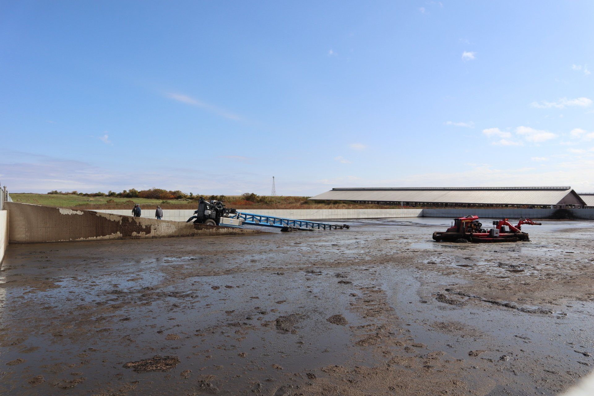 Flooded muddy field with a tractor and blue boat-like equipment under a clear sky