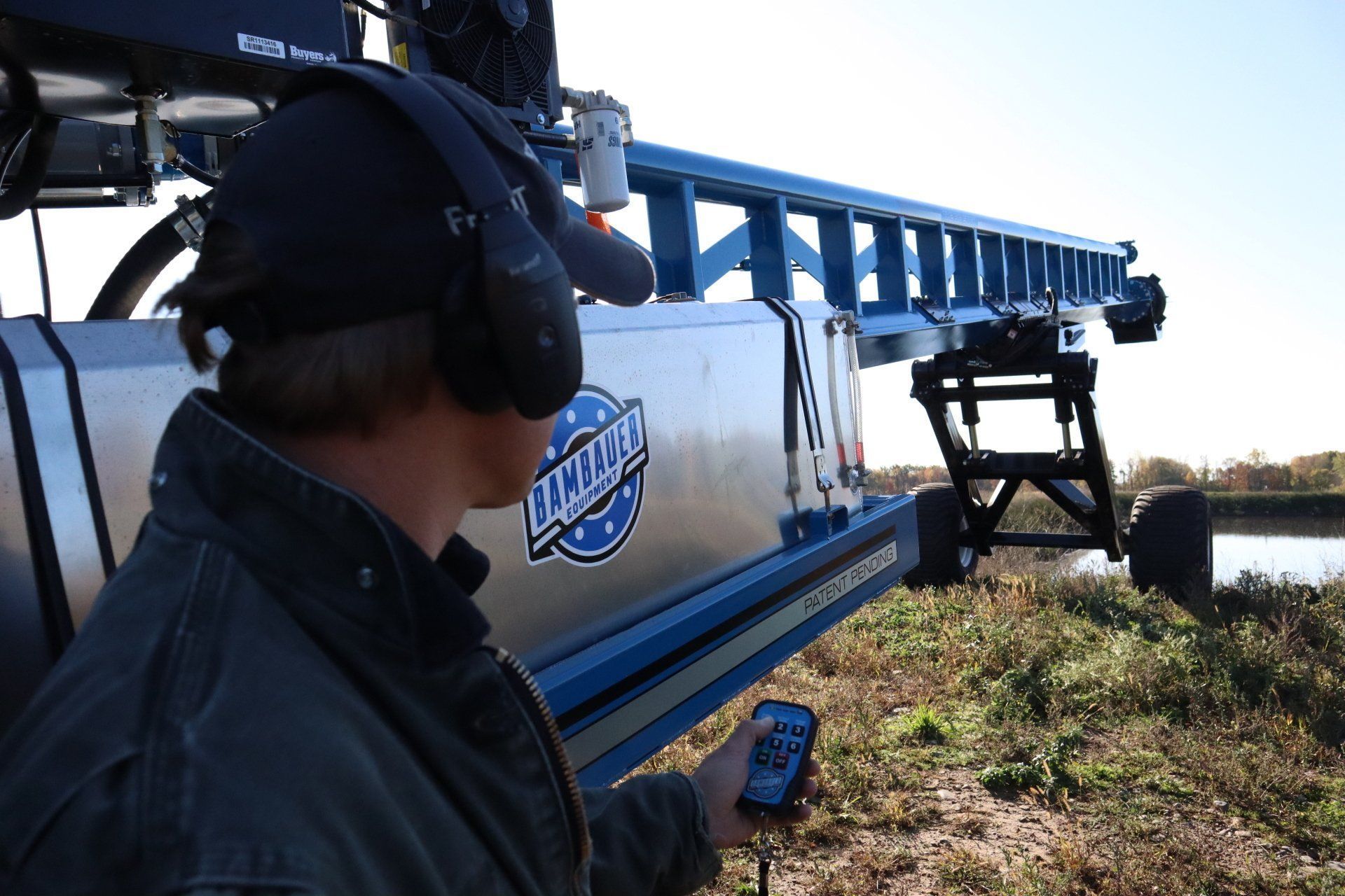 Person in headset beside a blue agricultural sprayer in a field at sunset