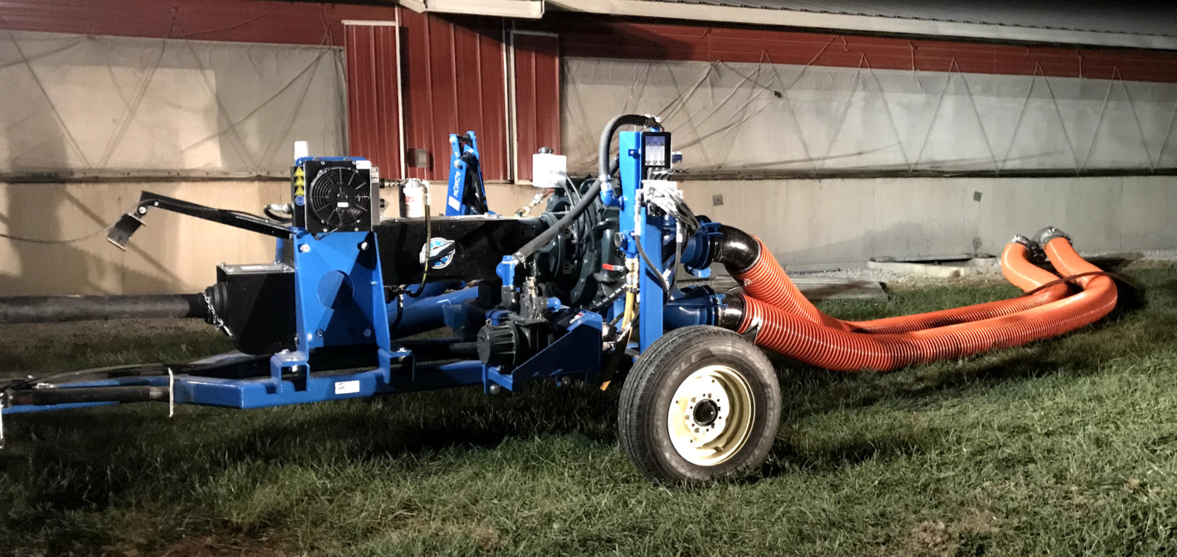 Blue farm machine with orange hose attachment parked indoors on a concrete floor