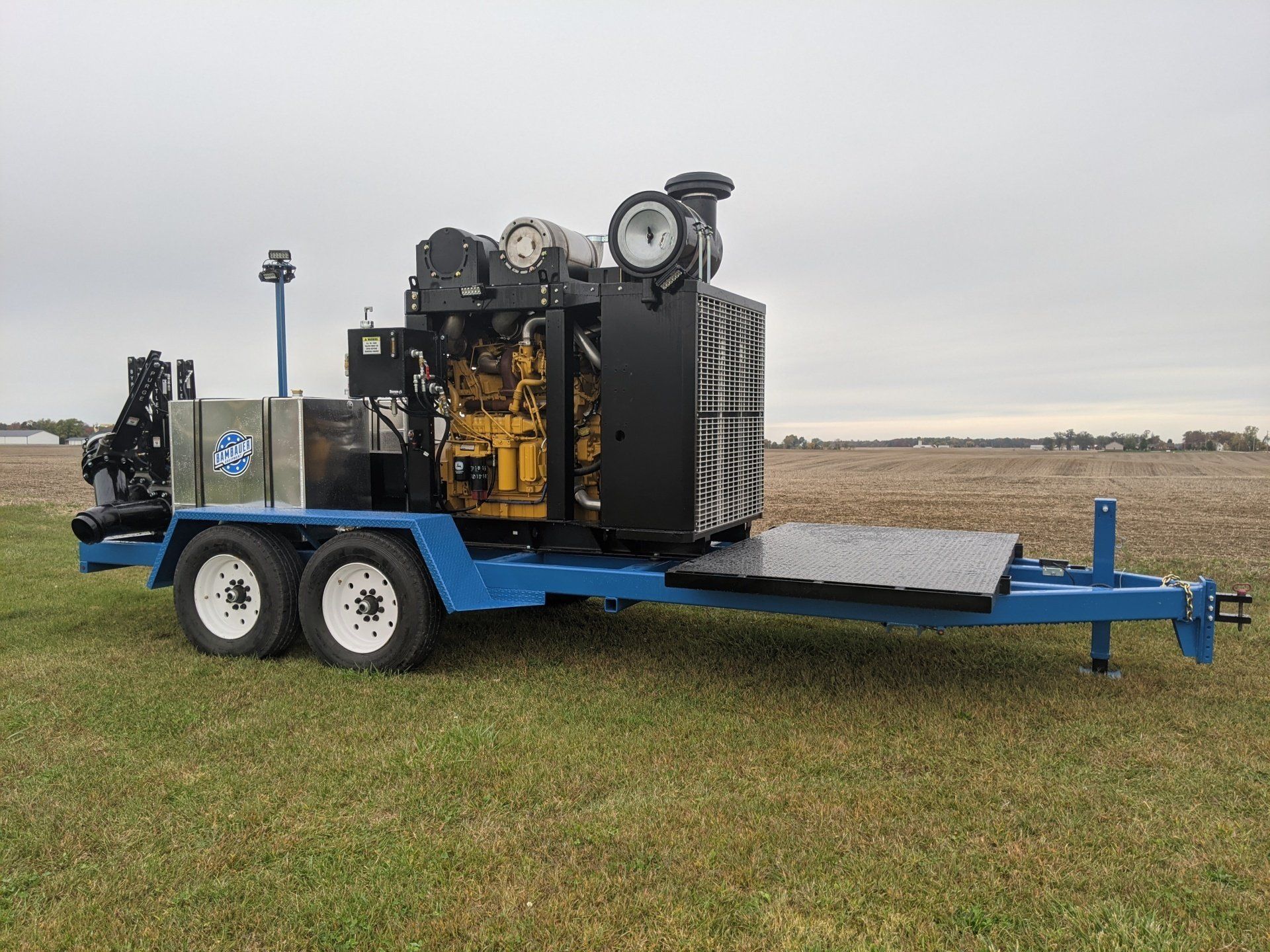 Blue trailer carrying a black industrial machine on a grassy field under an overcast sky