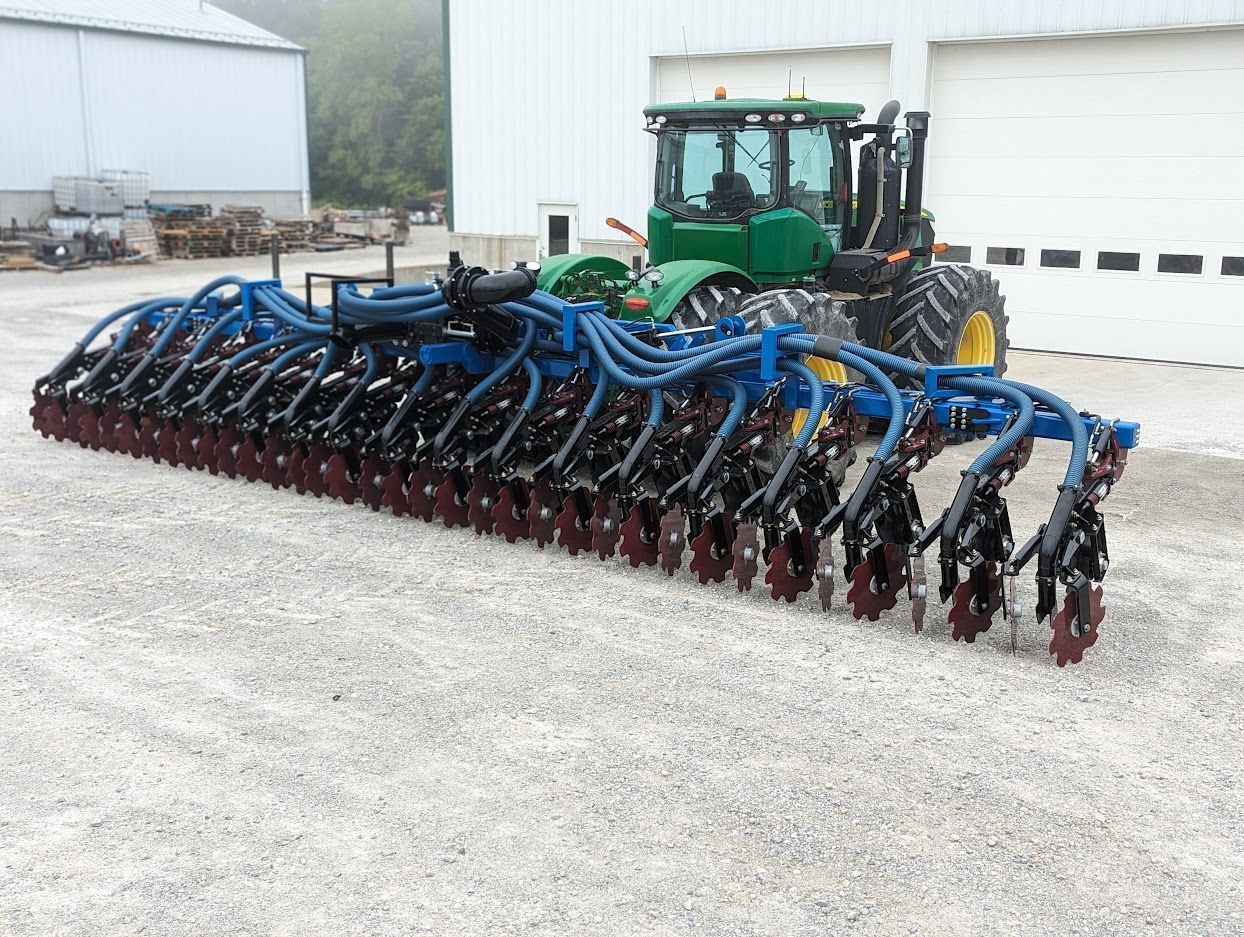Large green tractor pulling a wide blue and red farm implement on a gravel lot