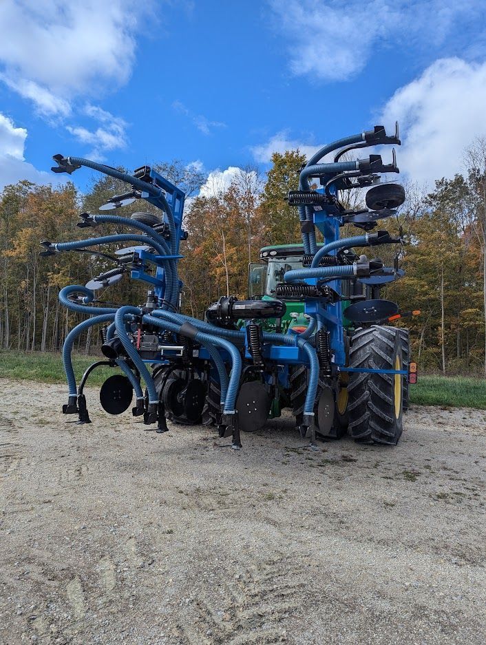 Blue agricultural machinery parked on gravel beside trees in autumn