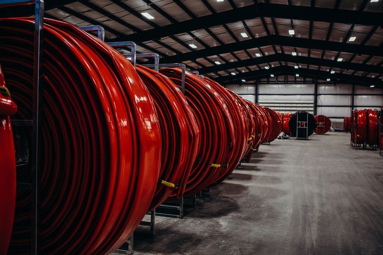 Rows of large red industrial coiled hoses stored in a warehouse aisle