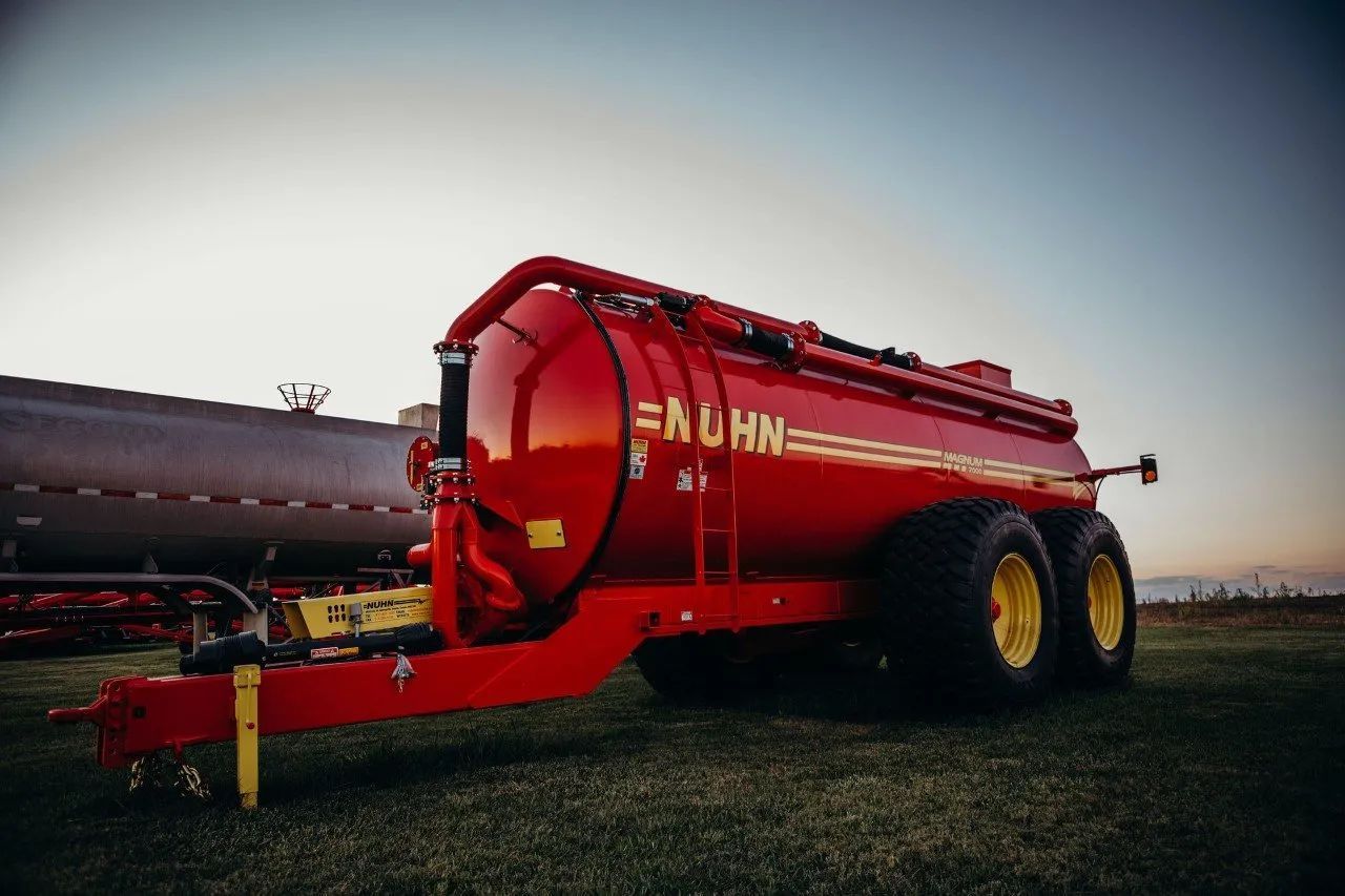 Red agricultural tanker trailer with yellow wheels in a field at dusk