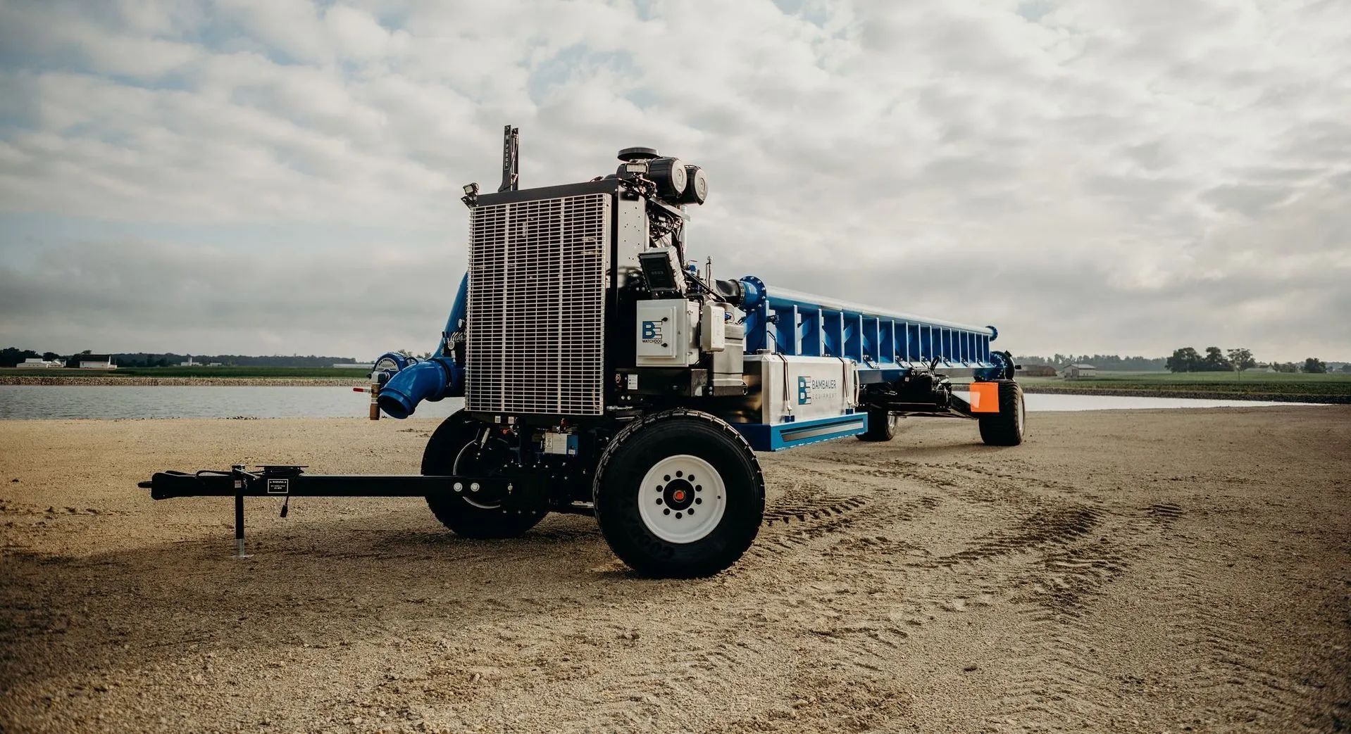 Blue agricultural sprayer tractor parked on a gravel field under a cloudy sky