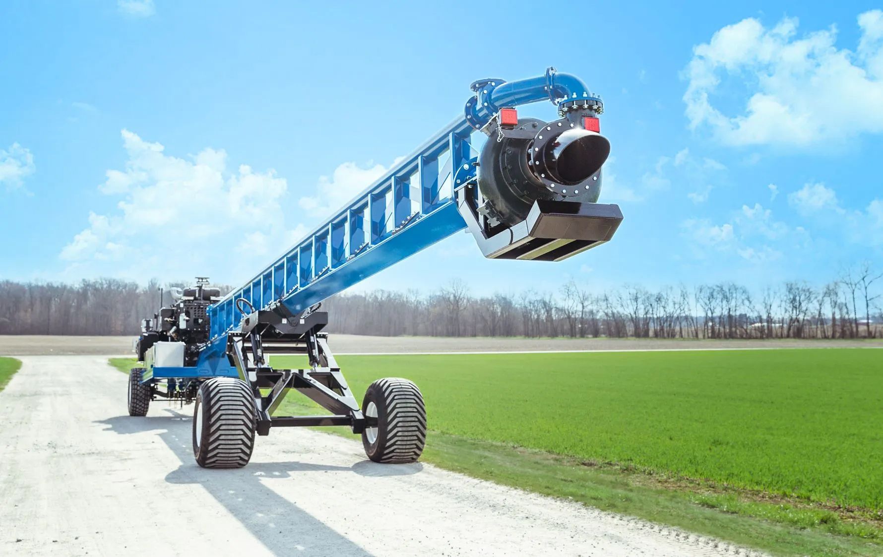 Blue agricultural boom sprayer on a field road under a bright sky