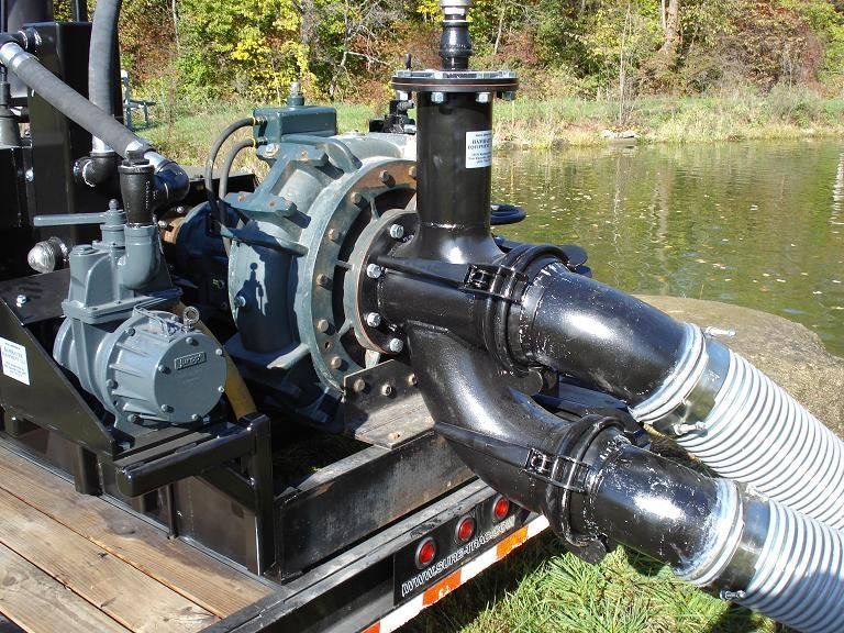 Industrial pump with large hoses mounted on a trailer beside a pond.