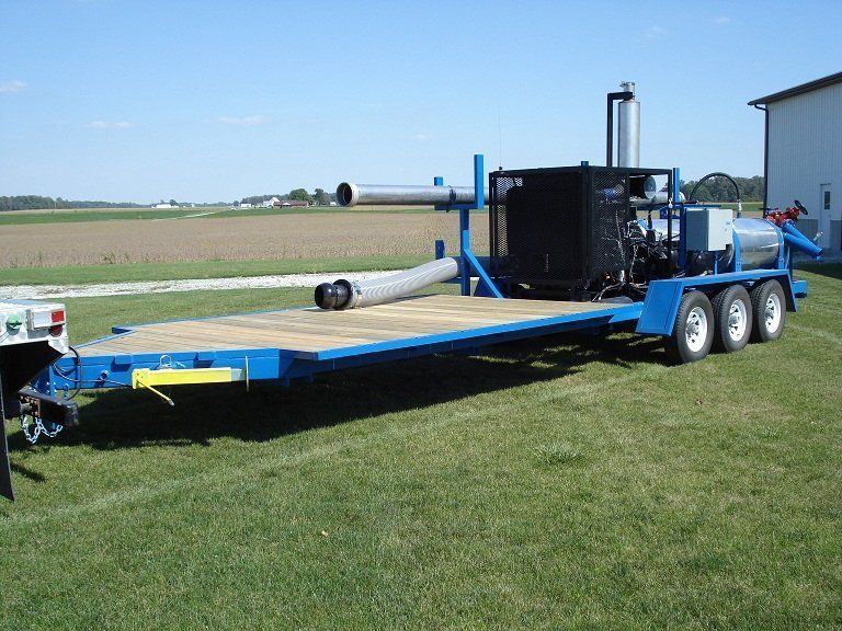 Blue flatbed trailer with black industrial equipment parked on grass in a field