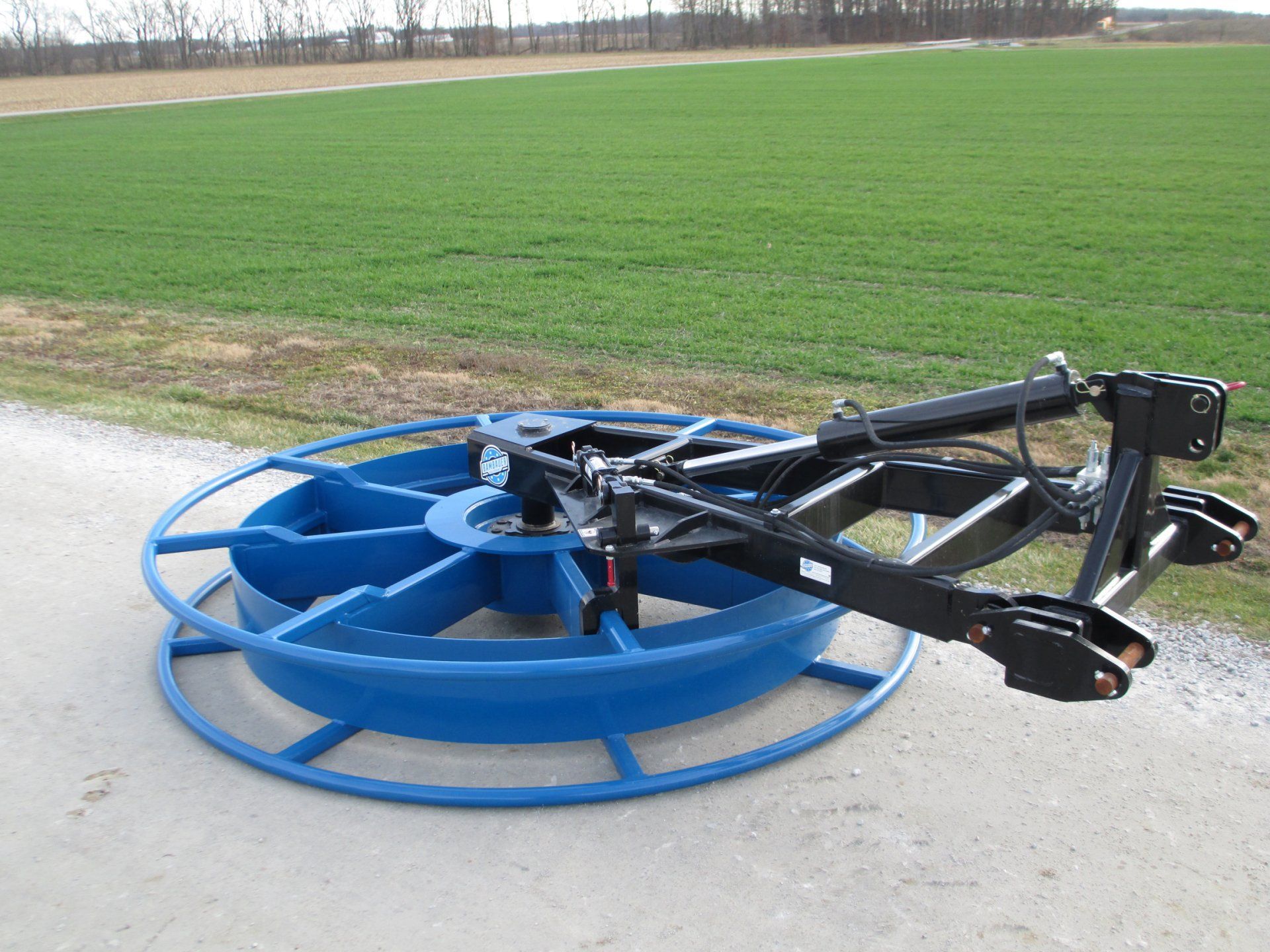 Blue agricultural implement on a paved road beside a green field