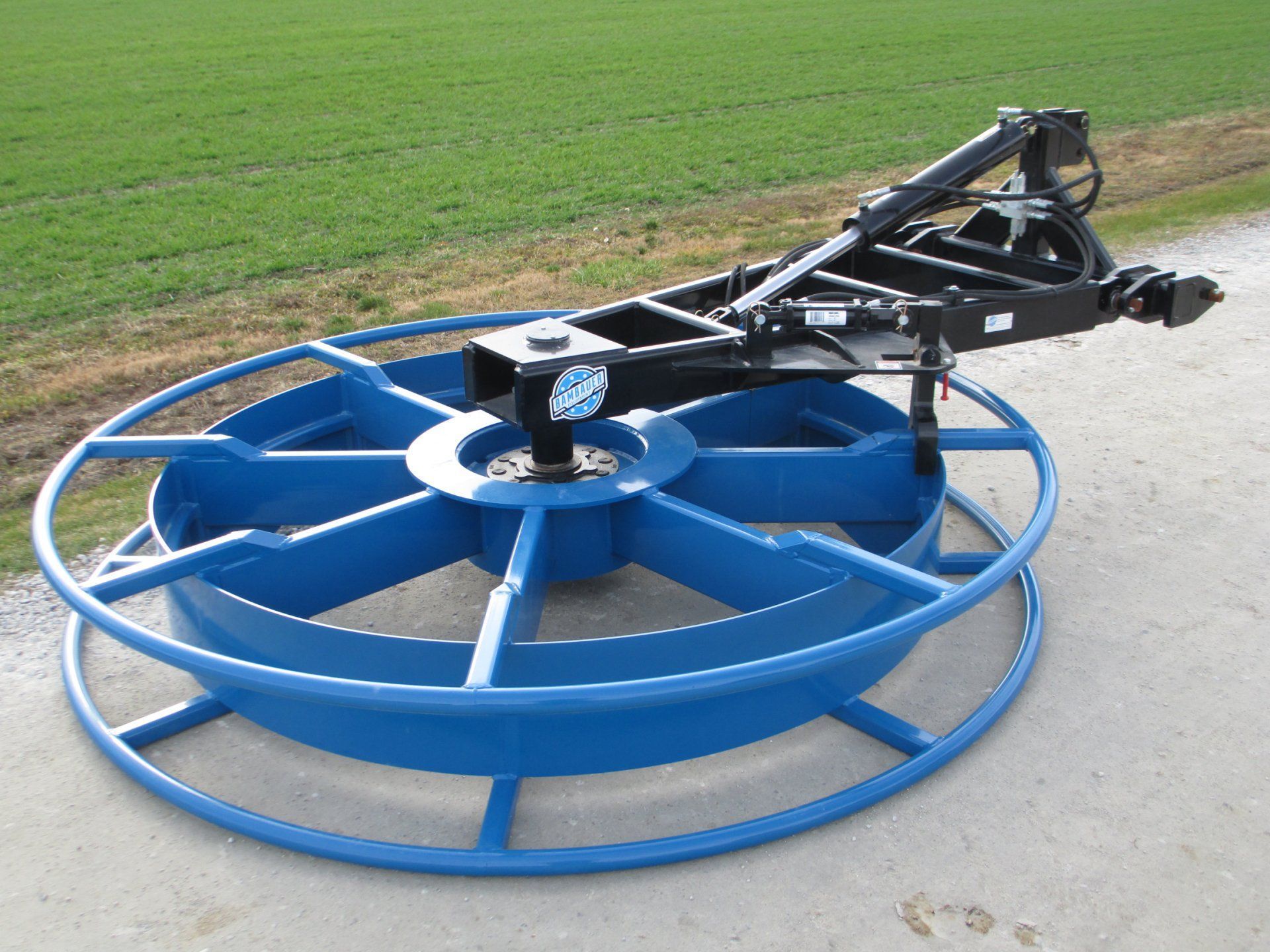 Blue agricultural mower attachment on grass beside a paved road