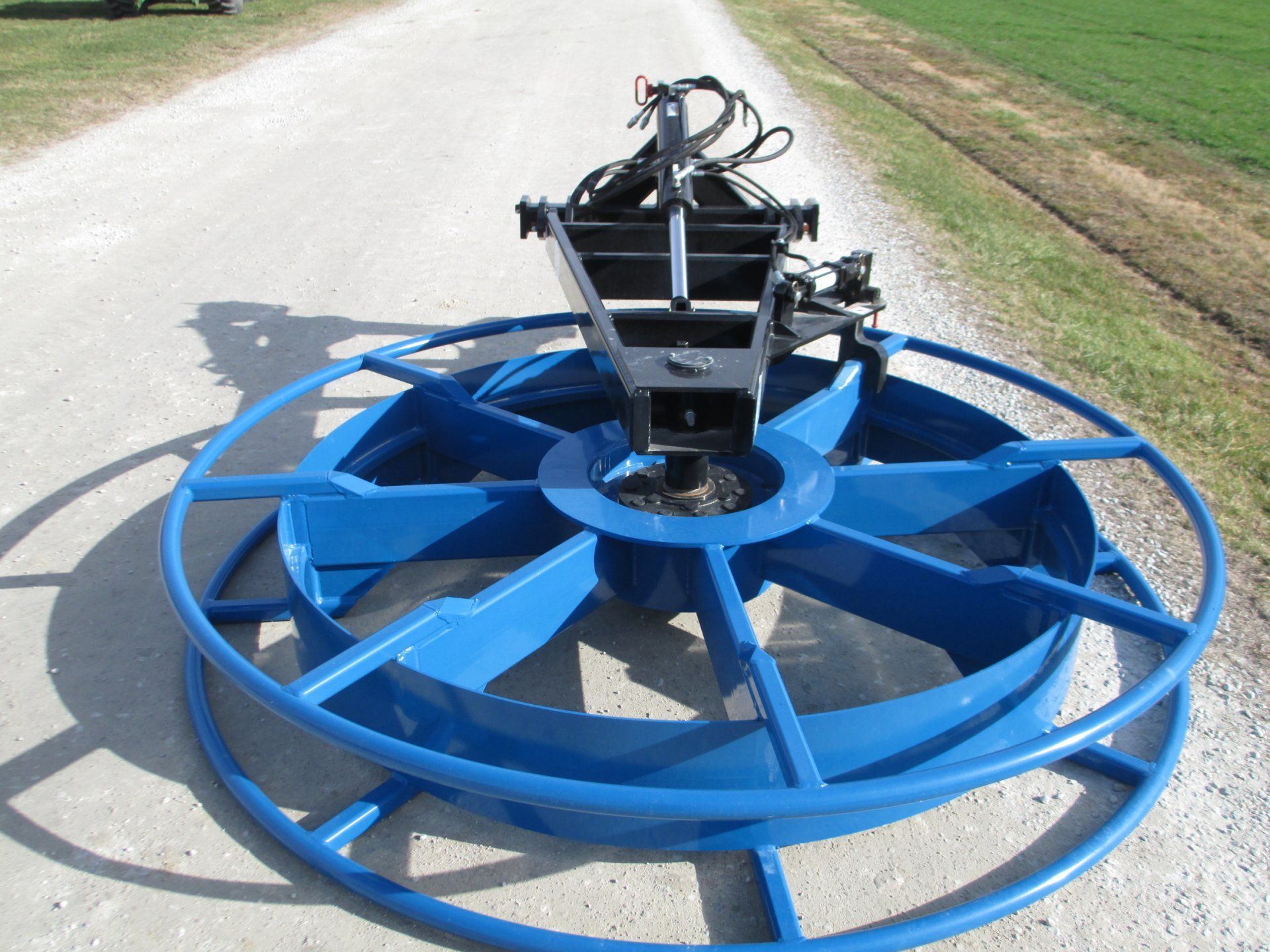 Blue farm implement with large circular wheels on a paved road beside a grassy field
