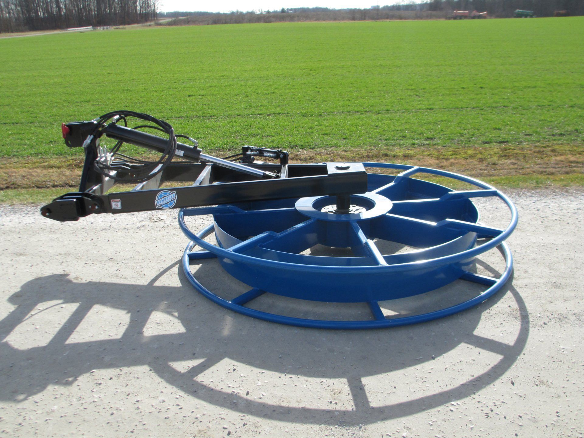 Blue agricultural wheel attachment in a field, with black metal frame and green crops in the background