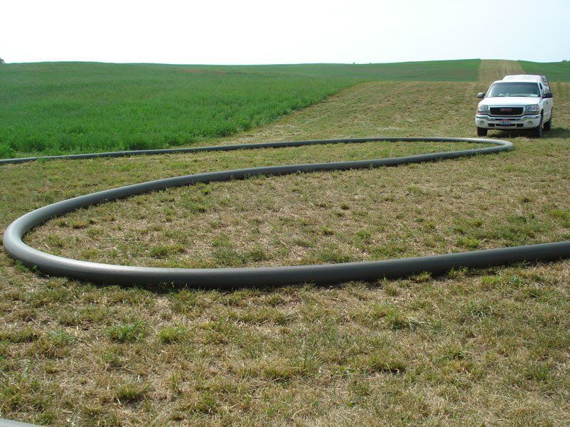 White car on a grassy field beside a large black hose or pipe under cloudy skies
