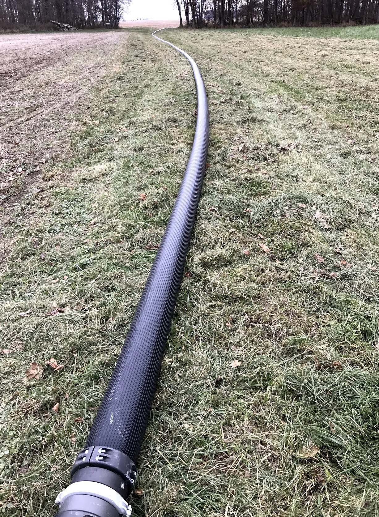 Black corrugated hose laid across a grassy field toward a tree line