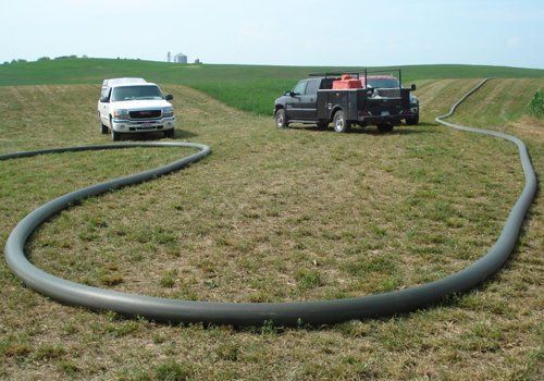 Two pickup trucks in a grassy field with a large hose or pipe laid in a loop between them