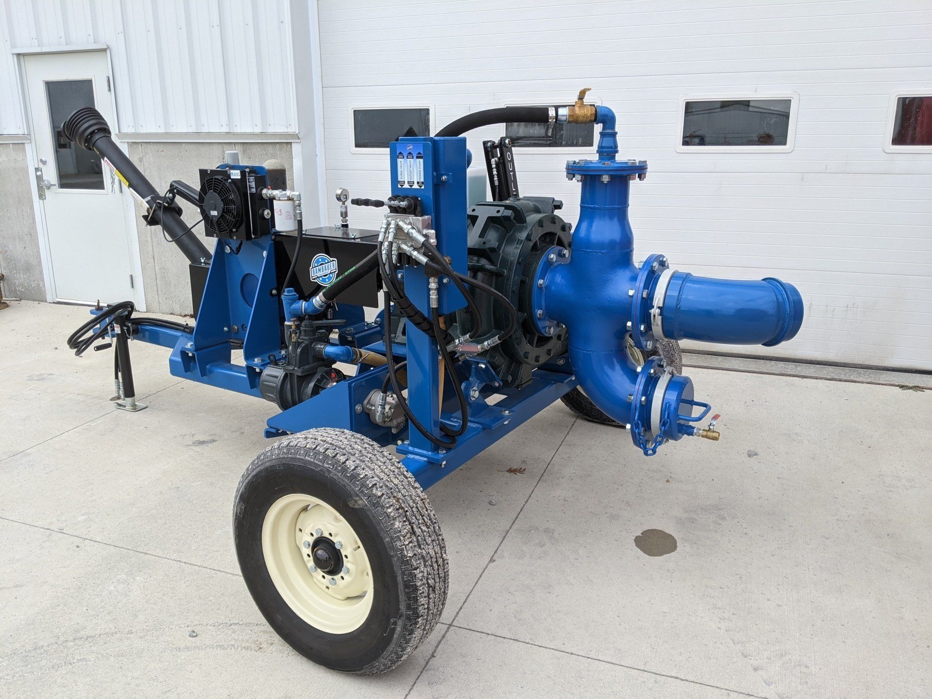 Blue industrial machine on a wheeled frame parked outside a building with garage doors.