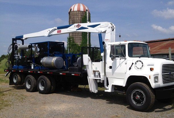 White utility truck with mounted boom arm and equipment parked outdoors near a striped water tower