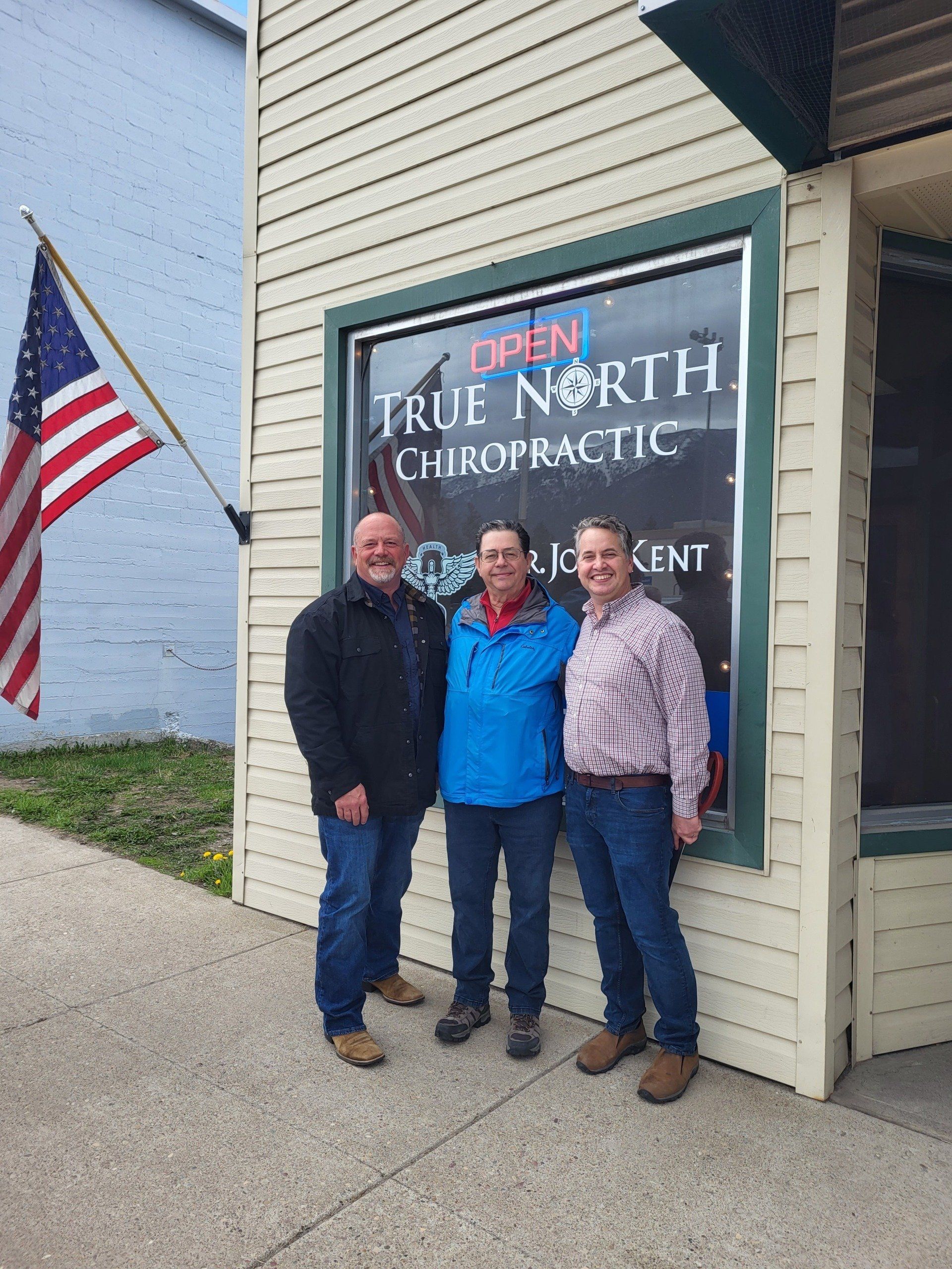 Three people are posing for a picture in front of a chiropractic office.