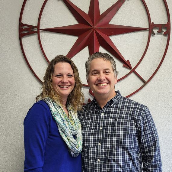 A man and a woman are posing for a picture in front of a compass on the wall