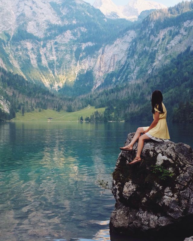 A woman in a yellow dress is sitting on a rock overlooking a lake