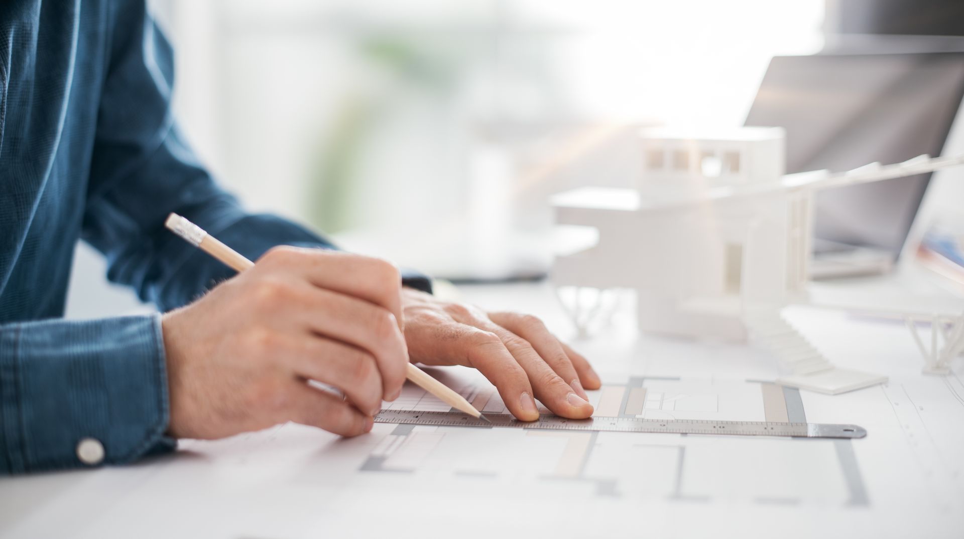 A man is sitting at a table drawing a house with a pencil.