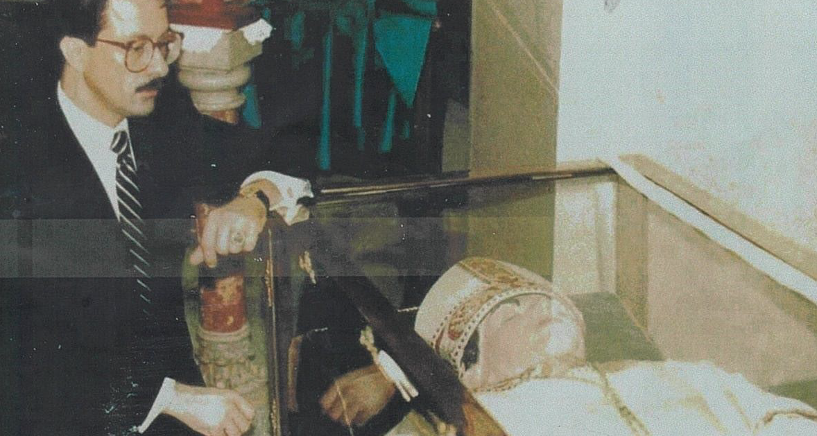 A man in a suit and tie is standing next to a woman in a coffin.