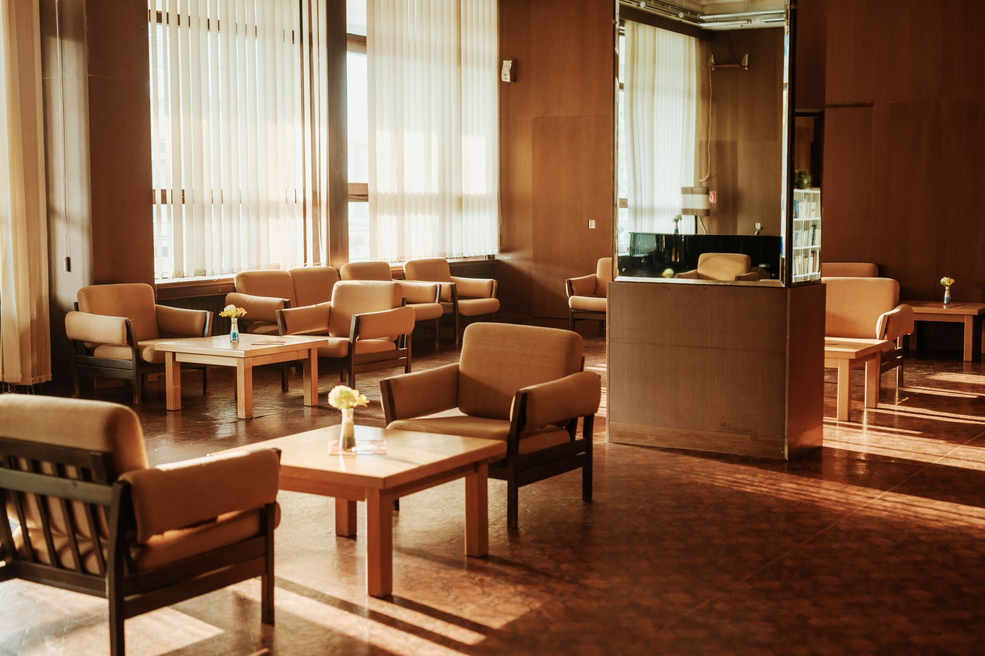 Warm-toned hotel lounge with brown chairs, tables, and sunlight through tall windows.