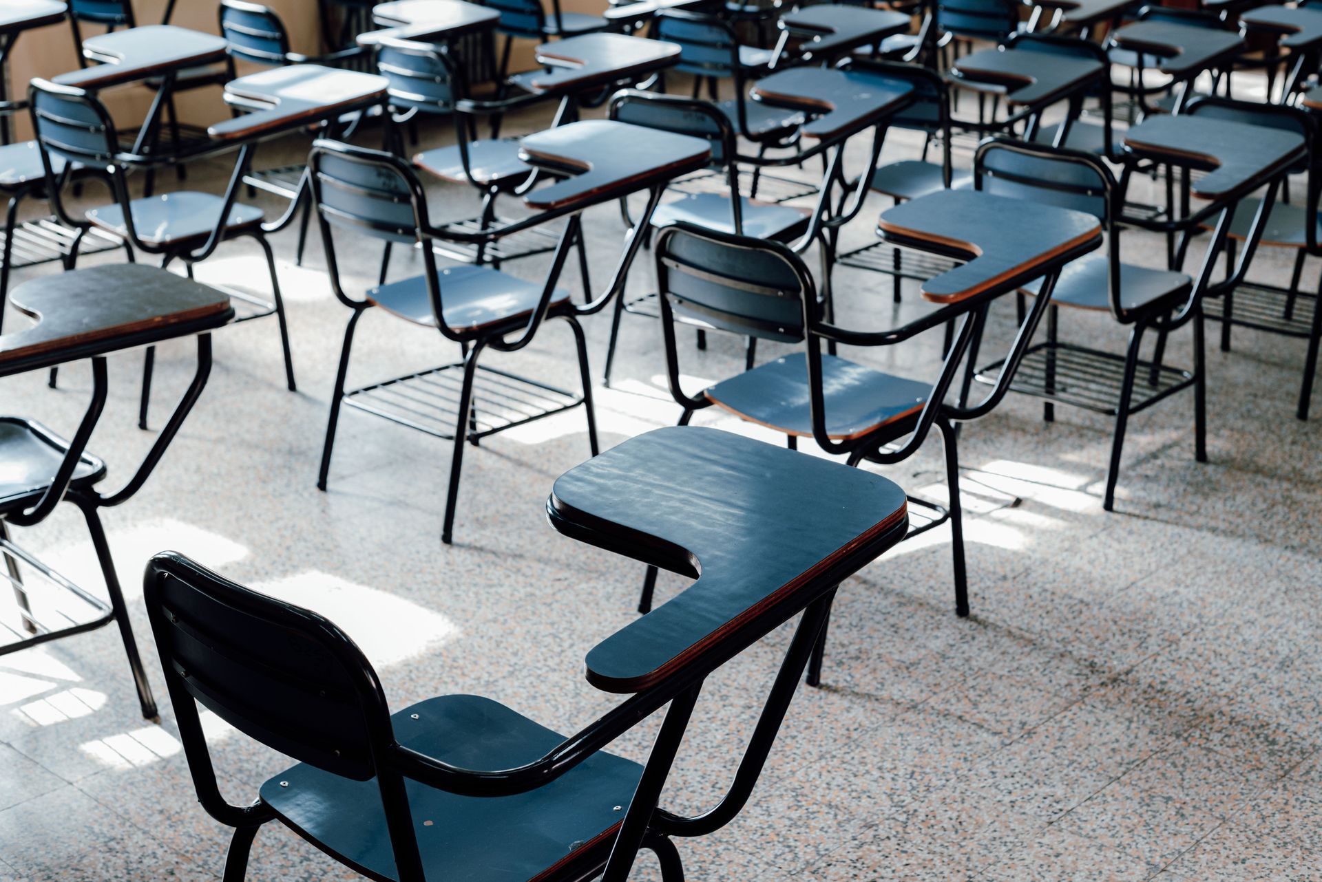 Empty classroom with rows of blue chairs and desks on a tiled floor