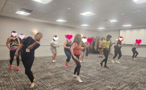 Group fitness class practicing dance moves in a bright studio with carpeted floor and ceiling lights
