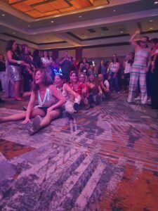People dancing in a hotel ballroom under purple lighting, with spectators around the edge.