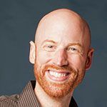 Smiling bald man with a red beard against a plain background