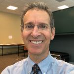 Smiling man in a blue shirt and tie in a classroom or meeting room
