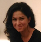 Smiling person with dark hair in a black top against a plain light background