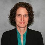 Portrait of a person with curly hair wearing a black blazer and teal shirt against a gray background